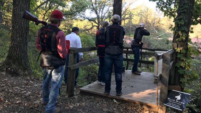 Trey Barnhart aims at clay targets with Aggie teammates and Coach Taylor watching. (Photo by Shotgun Sports athlete McKenna Darby)