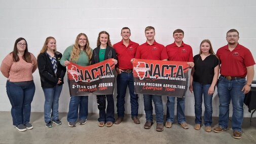 Group of NCTA crop judging team indoors holding NACTA conference banners.