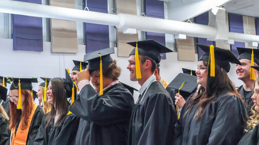 Graduates in caps and gowns standing in a brightly lit ceremony hall.