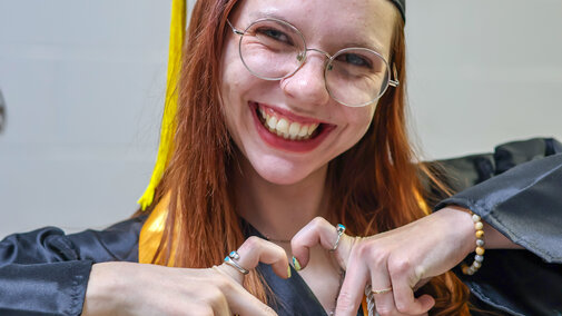 Graduate in cap and gown making a heart shape with hands.
