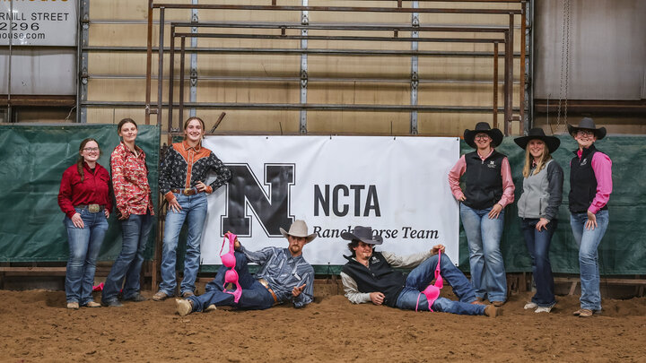 NCTA Ranch Horse Team posing in front of a banner in a barn setting.