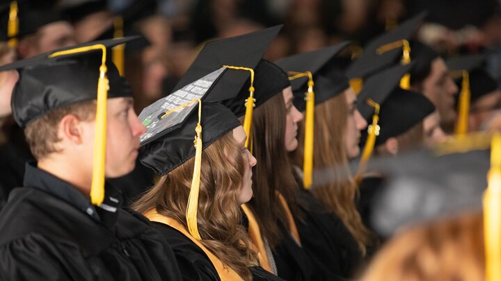 Graduates in caps and gowns seated in rows during a ceremony.