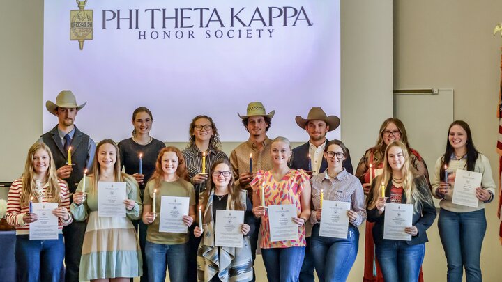 Group of people holding certificates and candles in front of a Phi Theta Kappa Honor Society banner.