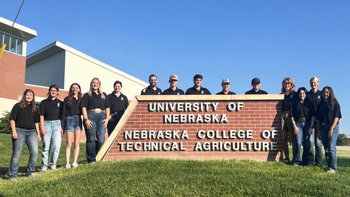 NCTA Resident Assistants in black shirts standing behind a the brick sign for Nebraska College of Technical Agriculture.